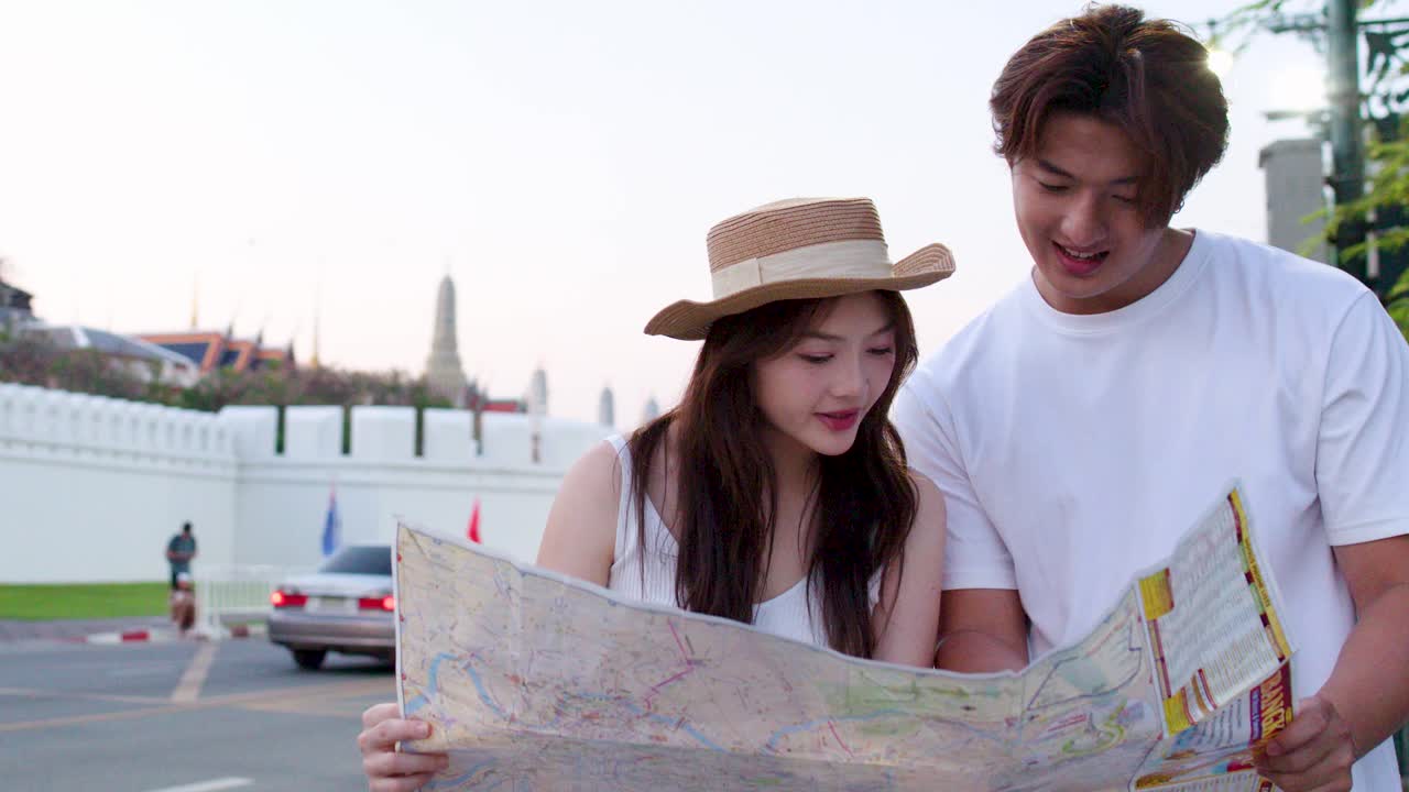 Coppia asiatica consulta una mappa all'aperto, con una luce soffusa al tramonto e un palazzo sullo sfondo, un momento di viaggio spontaneo.