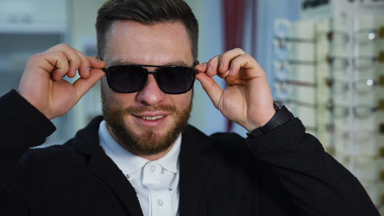 Facial portrait of a man in new black glasses in the shop. Happy businessman in sunglasses looking at camera. Man choosing new glasses in the optical store.