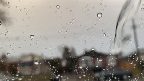 Fondo-De-Ventana-Lluviosa-Con-Gotas-De-Lluvia-Fluyendo-En-Su-Superficie-Con-Casas-Urbanas-Como-Fondo-Borroso,-Estado-De-ánimo-Triste