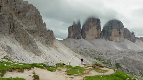a man standing on the edge overlooking tre cime di lavaredo or three peaks limestone face partially covered in clouds, dolomites, drone shot