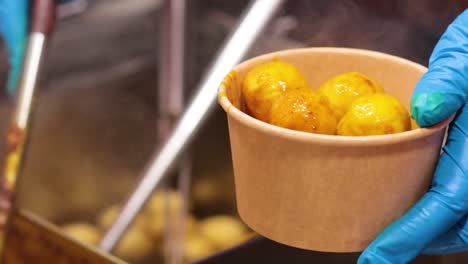 hand holding a paper cup of hot har gow dumplings