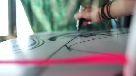 low angle close up of designer painting with black marker on white surfboard,slow motion