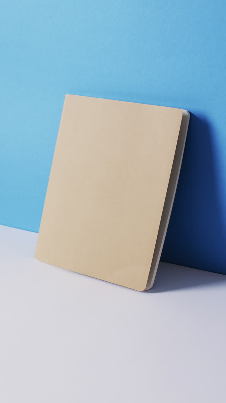 Vertical video of closed beige book leaning on wall with copy space in slow motion