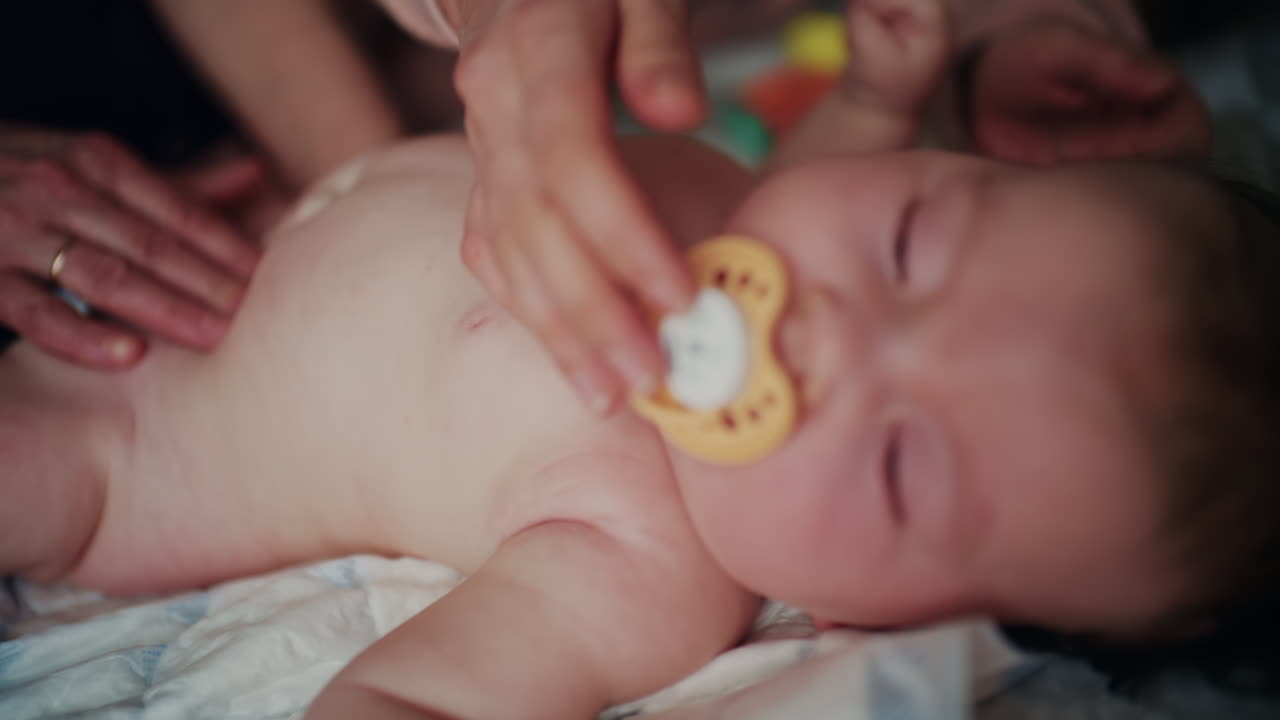 Close up of caregiver hands gently massaging baby belly while infant rests calmly with pacifier