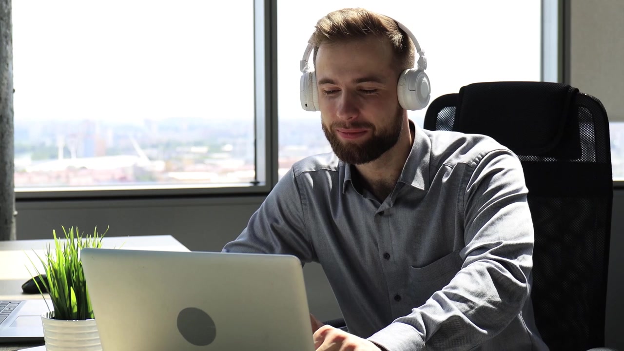 Happy Man in Headphones Waving During Video Call on Laptop