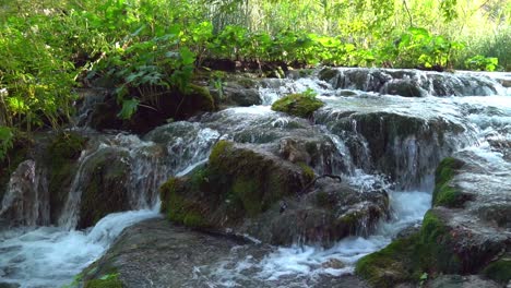 cascada de agua a lo largo de una serie de grandes rocas cubiertas de musgo en el parque nacional de los lagos de plitvice en croacia, europa a ¼ de velocidad