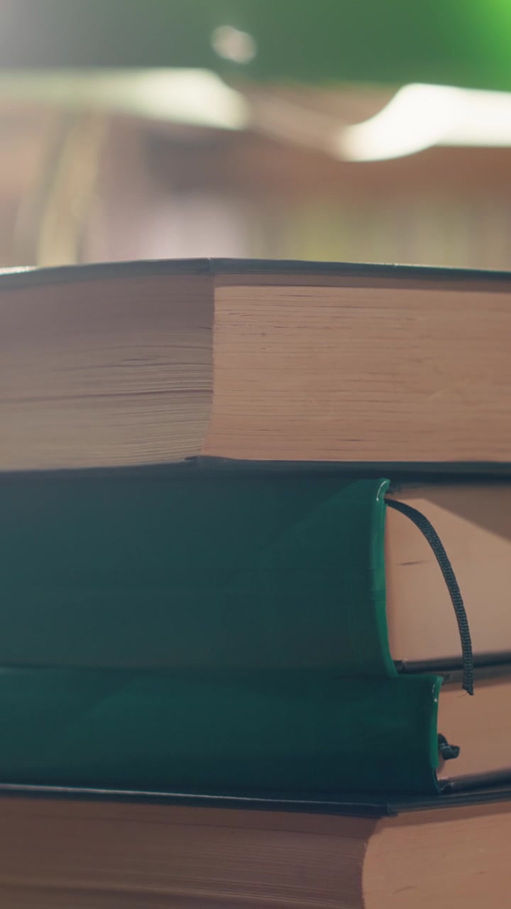 Vertical Video Stack of books on desk in quiet university library with warm lighting