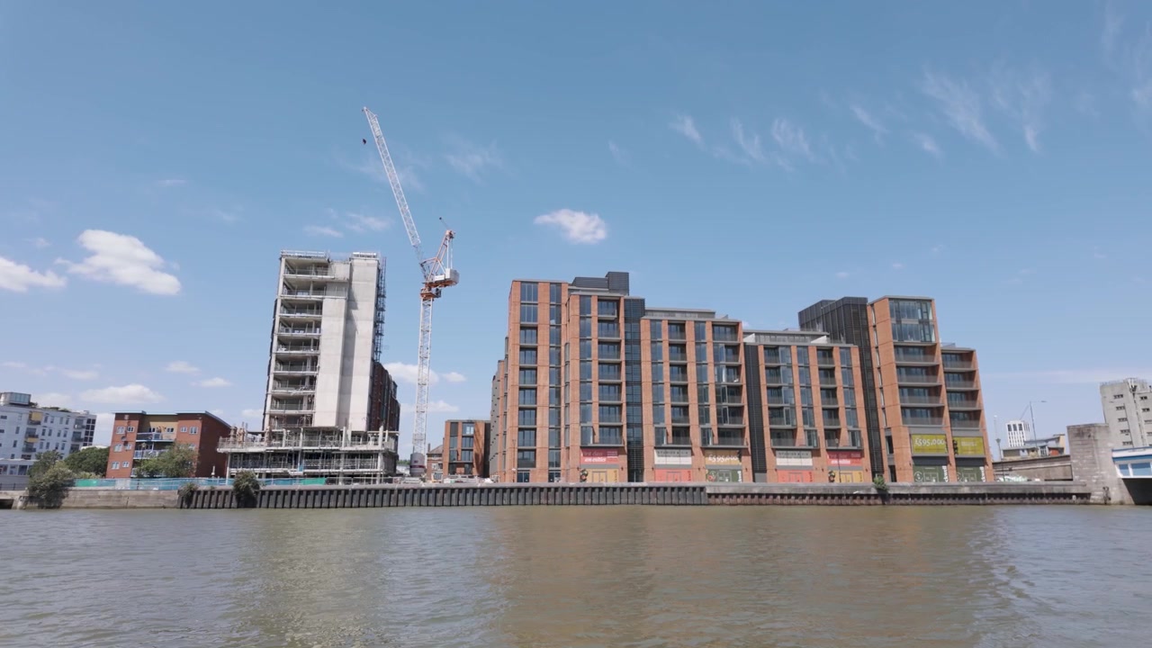 Nuovi edifici residenziali in mattoni e vetro in costruzione accanto a una gru a torre sulla riva del fiume, visti dall'acqua