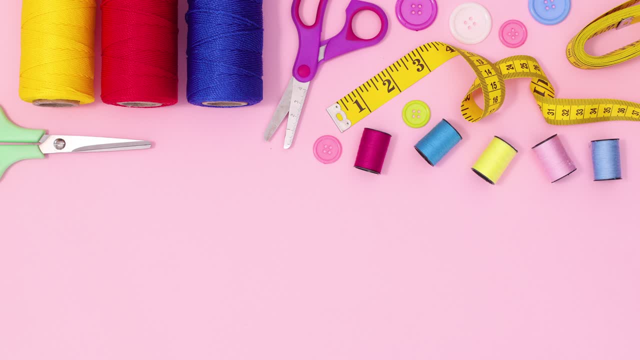 Creative sewing and knitting craft items appear on top of pastel pink background. Stop motion flat lay