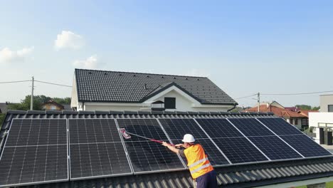 male worker cleaning solar panels on roof by wiping with wet soft cloth