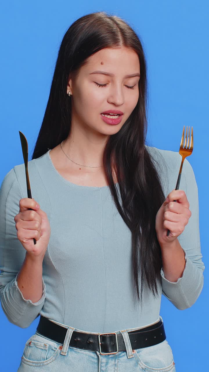 ⁇ 주린 여자가 저녁 식사 식사 접시를 위해 기다리고 불안으로 식구 포크 칼을 들고 있습니다.