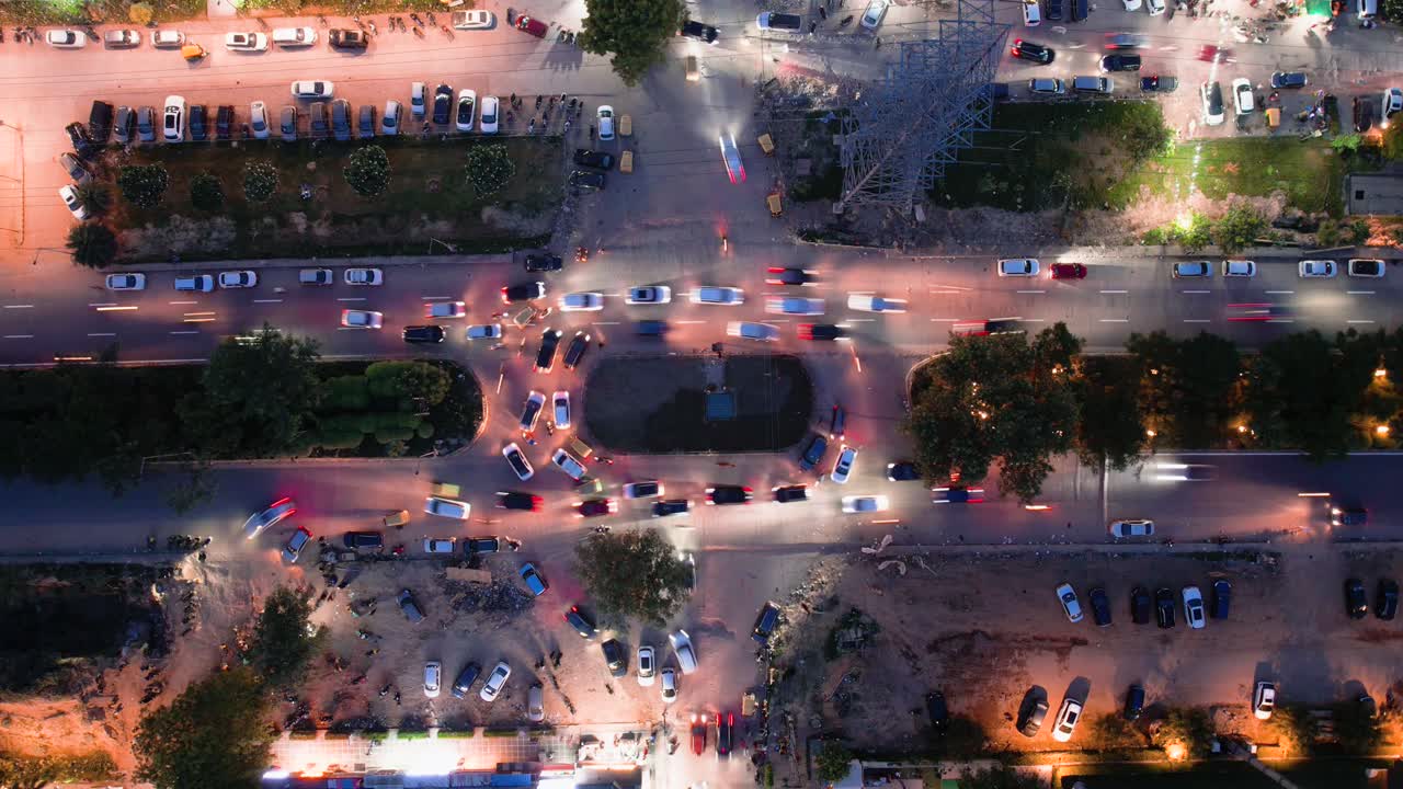 Aerial drone hyperlapse shot straight down into a busy roundabout turn with cars passing and parking in nearby markets
