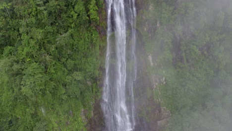 aerial rising over las lajas misty waterfall surrounded by green dense rainforest and clouds, san luis morete, costa rica