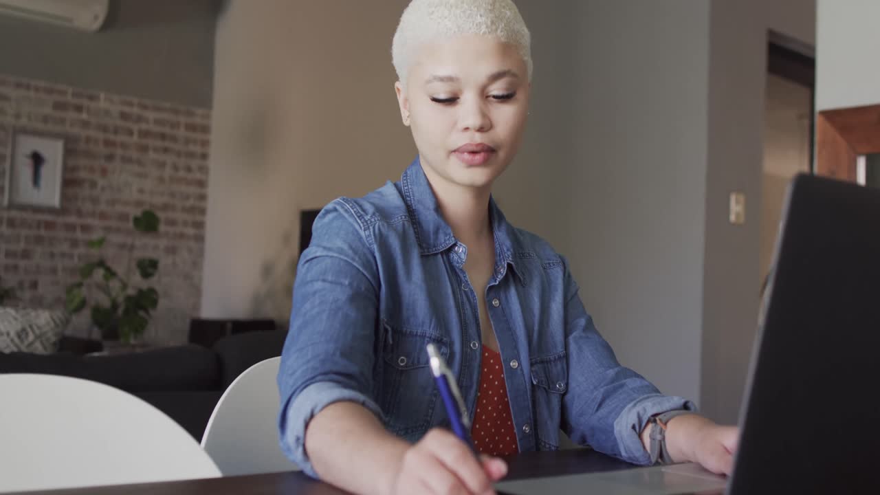 Busy biracial woman working at home with laptop in slow motion