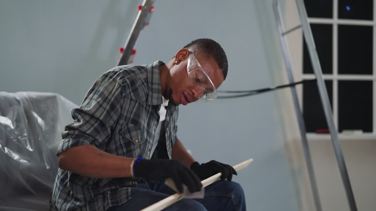 Young black worker with goggles polishes wooden plank