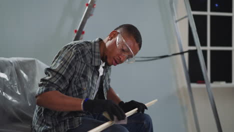 Young-black-worker-with-goggles-polishes-wooden-plank