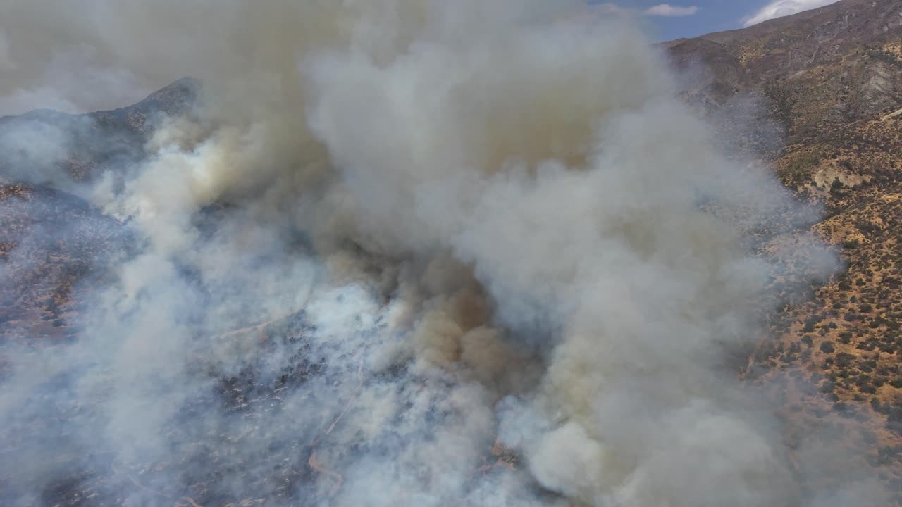Ripresa aerea dall'alto verso il basso con drone di un'intensa nuvola di fumo bianco che si solleva da un incendio su un pendio montuoso arido in Cile e video 4K