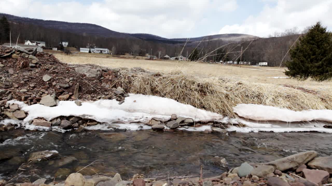 muñeco lento a la derecha por un arroyo de agua dulce en las montañas catskill con un vecindario rural en el fondo