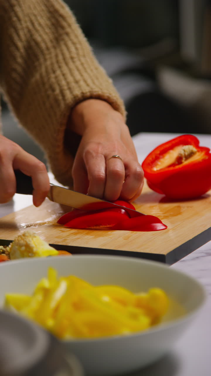 video vertical de cerca de una mujer en casa en la cocina preparando verduras frescas saludables para una comida vegetariana o vegana cortando pimientos rojos a bordo