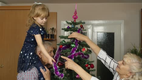 Kleines-Mädchen-Mit-Großmutter-Und-Großvater,-Die-Einen-Künstlichen-Weihnachtsbaum-Mit-Spielzeug-Dekorieren