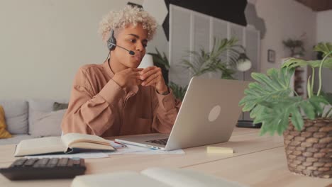 african female student wearing headset looking at laptop watching online webinar