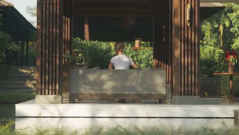 Elegant-woman-sitting-down-in-open-air-luxury-lounge-of-resort-in-morning