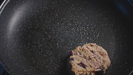 hand adding tuna fritters to an empty black pan and gently pressing them to make then flat