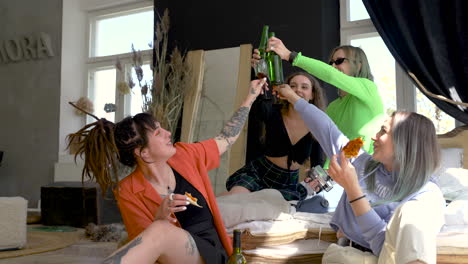 grupo de cuatro jóvenes amigas brindando con cervezas y vino mientras comen pizza en casa 1