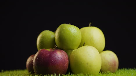 montón de manzanas frescas verdes y rojas sobre la hierba contra el fondo negro