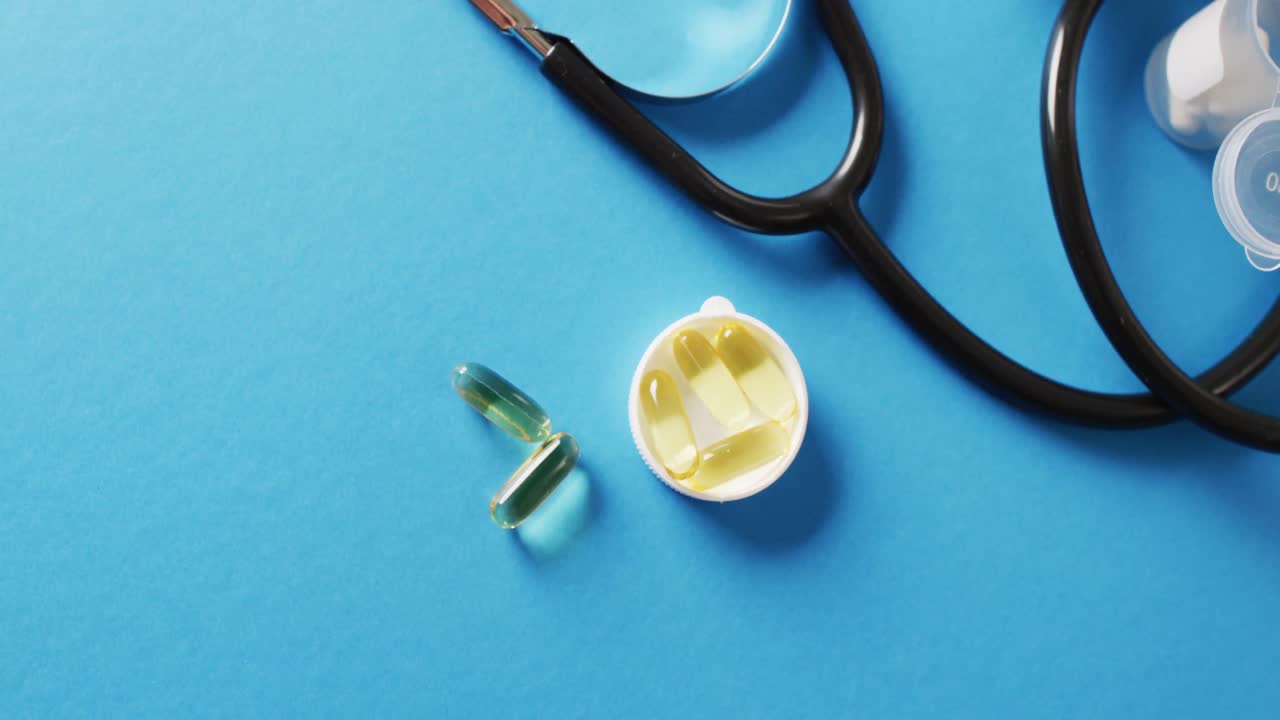 Video di stetoscopio con capsule di olio e pillole su sfondo blu con spazio per il testo