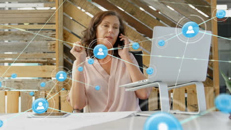 animation of network of profile icons over caucasian woman talking on smartphone at office