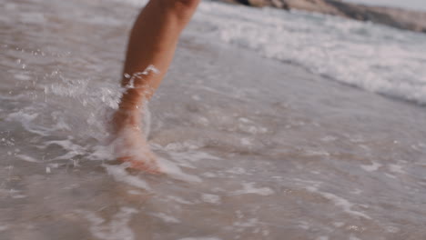 Cerrar-Los-Pies-De-Una-Mujer-Caminando-Descalzo-En-La-Playa-Disfrutando-De-Las-Olas-Salpicando-Suavemente-A-Una-Turista-En-Vacaciones-De-Verano