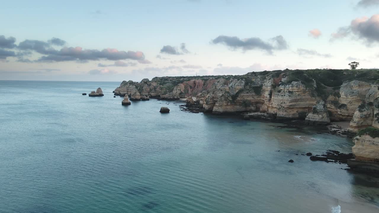 Aerial drone flies forward above rugged limestone cliffs and calm turquoise sea along Algarve coast near Lagos