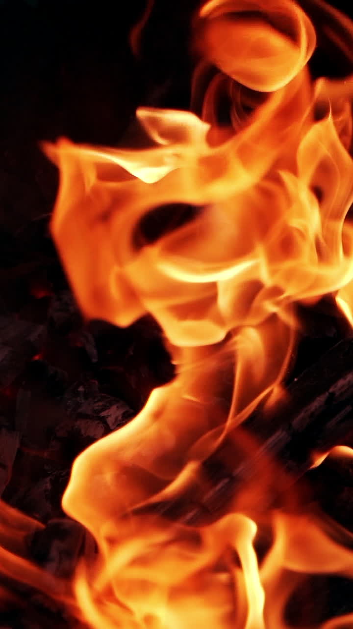 Orange flame on black firewood. Bright fire burning on black background outdoor. Detailed motion of burning logs. Vertical video