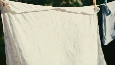 clothes hang on a line in a backyard, gently swaying in the wind. the bright sunlight illuminates the fabric, creating a tranquil atmosphere.