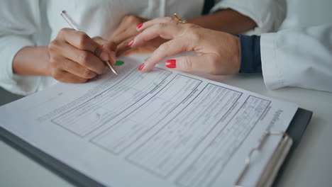 closeup patient writing form in healthcare clinic. woman hand pointing document