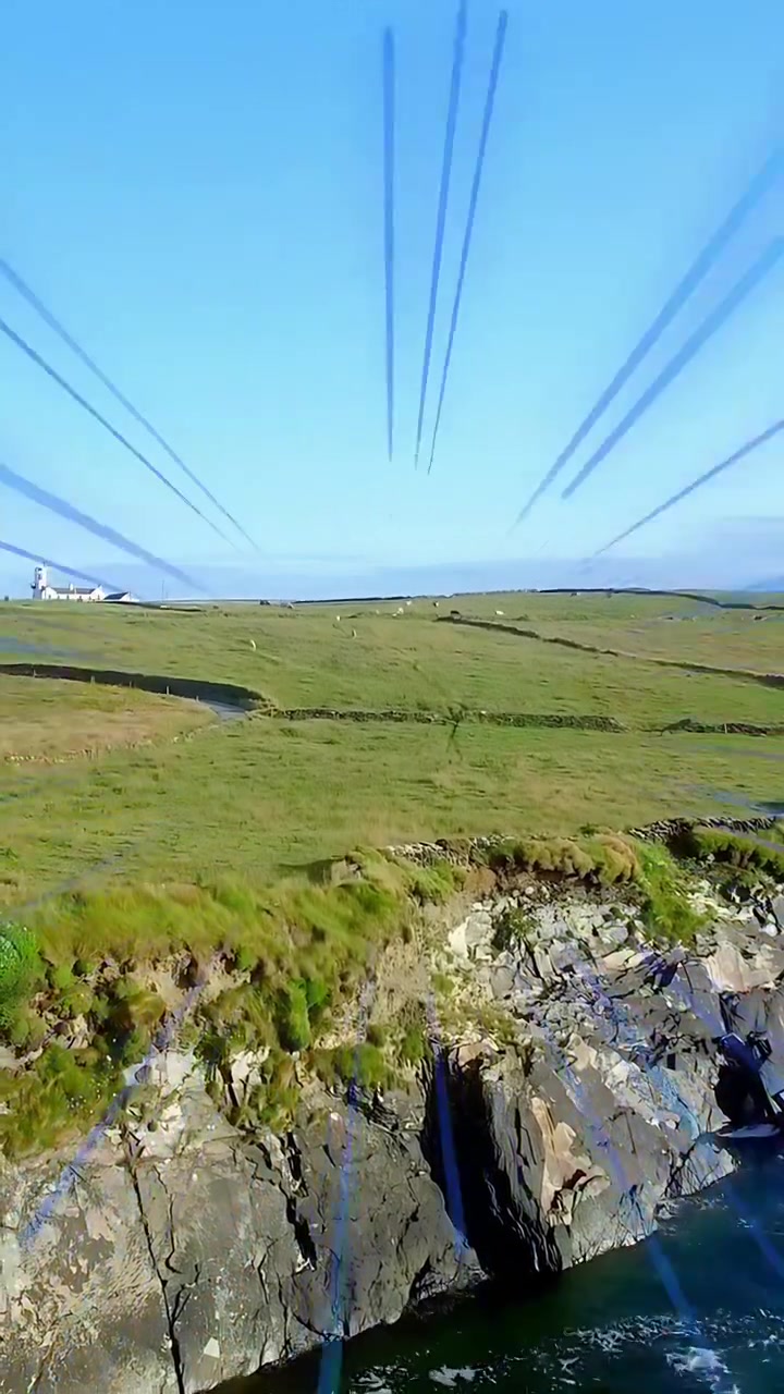 Vertical video: Cam moving behind cliff coast showing field blue rays growing to reveal lighthouse