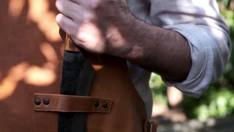 man puts large knife into a leather strap on an apron