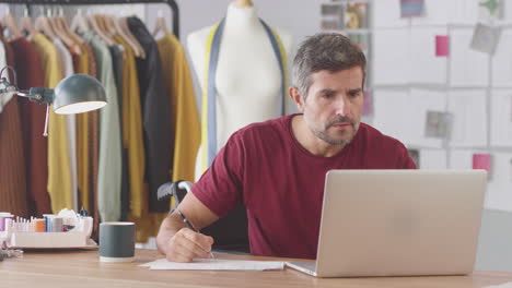 Mature-Male-Fashion-Designer-In-Wheelchair-In-Studio-Working-On-Laptop-Computer