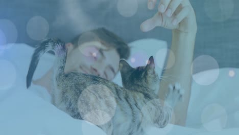 spots of light against caucasian man playing with his cat while sleeping on the bed at home