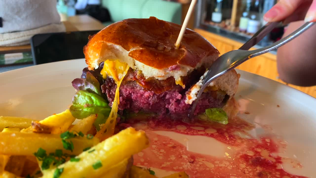 comiendo una hamburguesa con queso extra jugosa con queso cheddar, lechuga, bollo de brioche y papas fritas, restaurante de comida rápida, toma de 4k