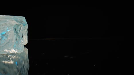 toma macro cinematográfica iluminada en azul de cuarzo blanco reluciente deslizándose lentamente sobre un fondo oscuro, capturada a través de un suave movimiento deslizante motorizado