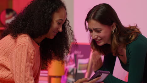 dos mujeres jóvenes riendo y mirando un teléfono juntas