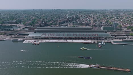 aerial view of boat sailing past amsterdam central station during clear sunny day with subtle zoom out