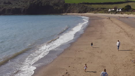 drone shot of family on vacation running along beach by breaking waves