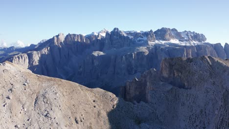 Aerial-drone-shot-flying-over-beautiful-mountain-ridge-of-Dolomites-with-snowcapped-view-at-the-background,-Northern-Italy