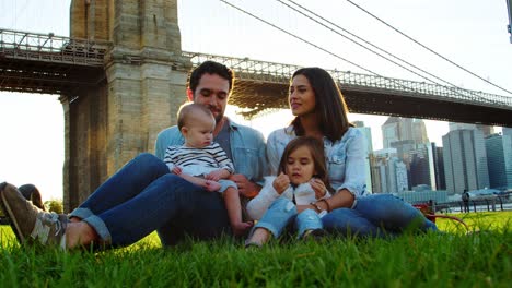 young family with daughters sitting by bridge in manhattan