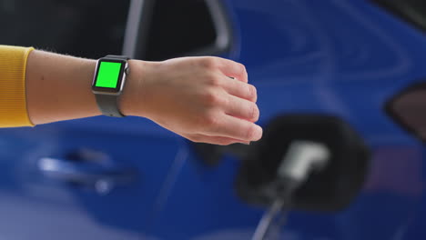 woman charging electric car with cable uses app on green screen smart watch to monitor battery level