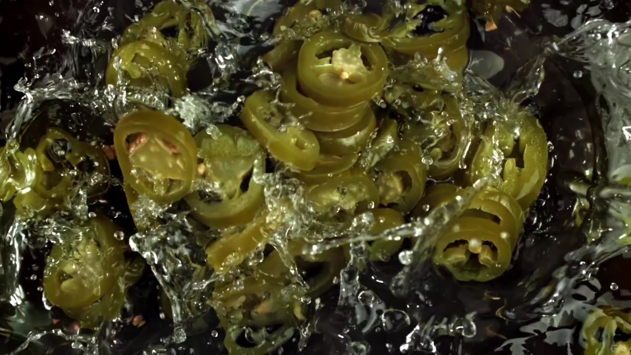Skiveskårne jalapeño-peberfrugter falder ned i vand i slowmotion