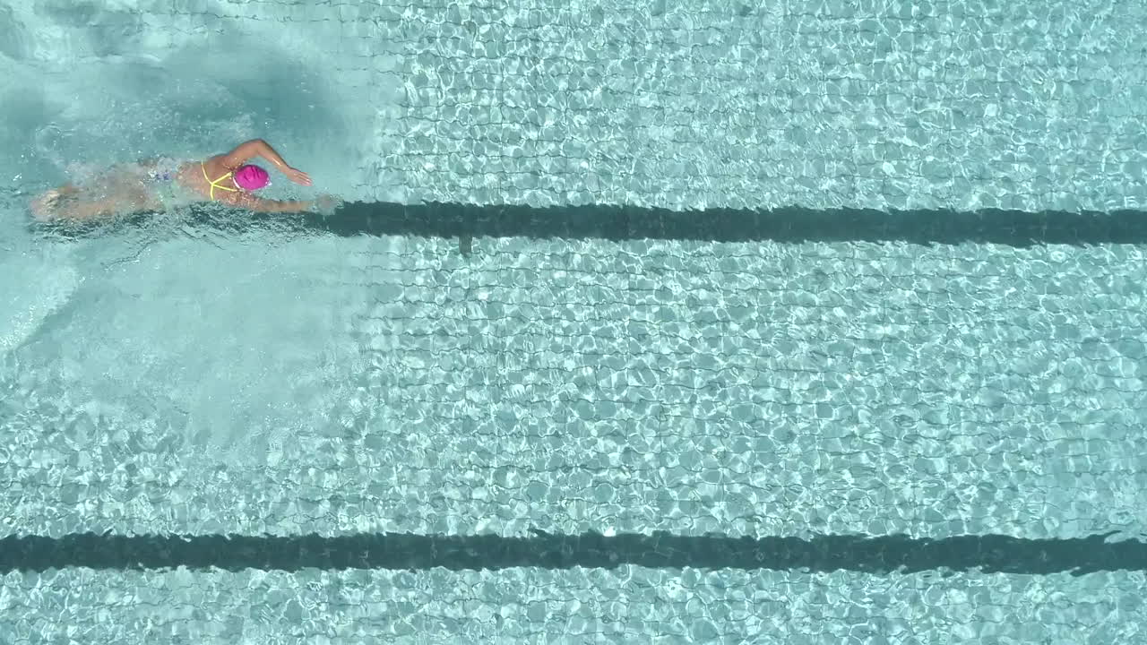 rekaman drone di atas kepala seorang perenang wanita yang menyelam ke dalam kolam renang terbuka dan berenang sebagai bagian dari pelatihan triatlonnya